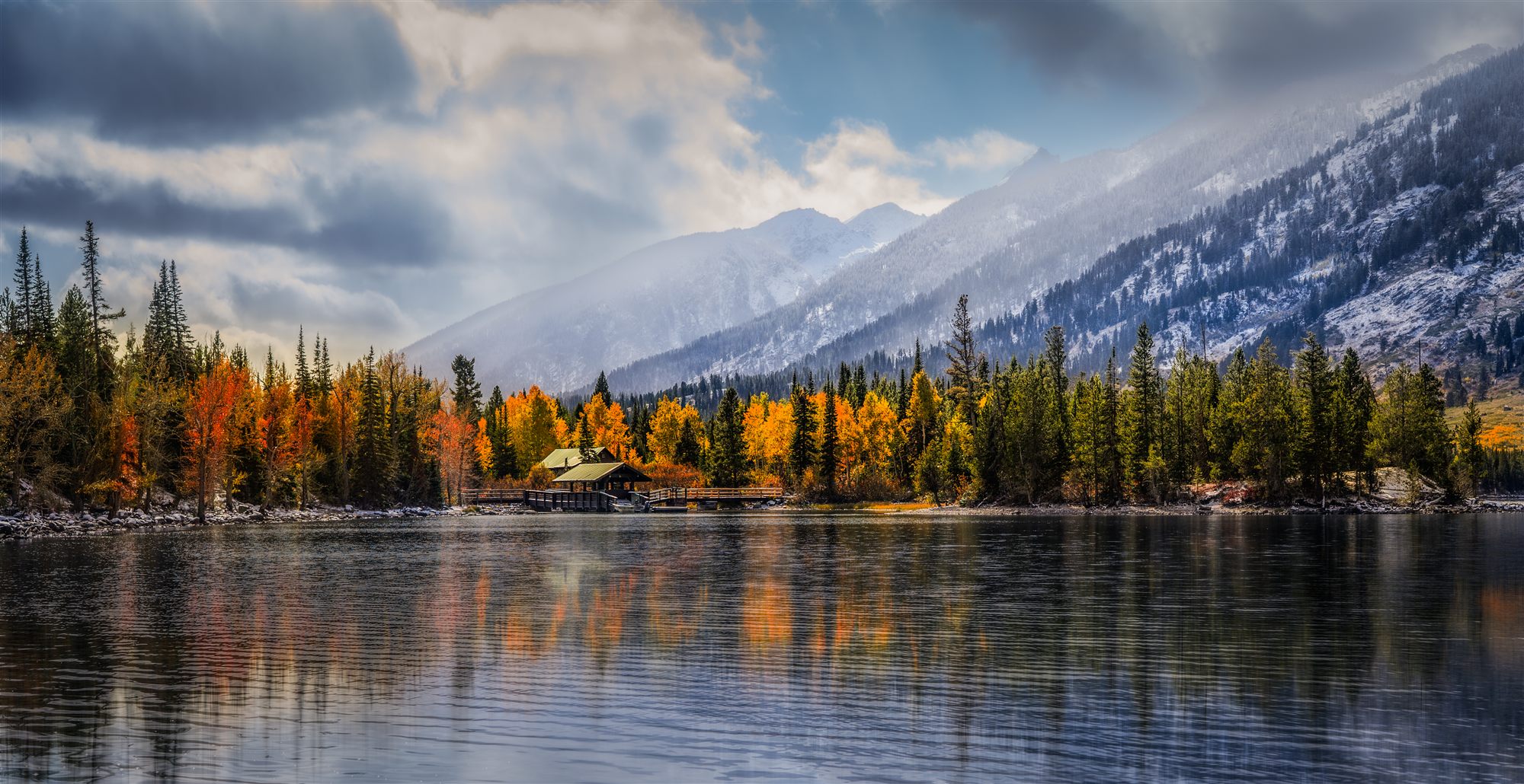 Alpine lake mirroring a cabin, gold aspens, and snow-dusted Teton peaks