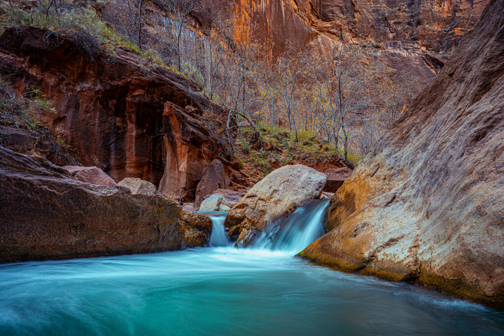 Turquoise river folding over a ledge between red sandstone canyon walls