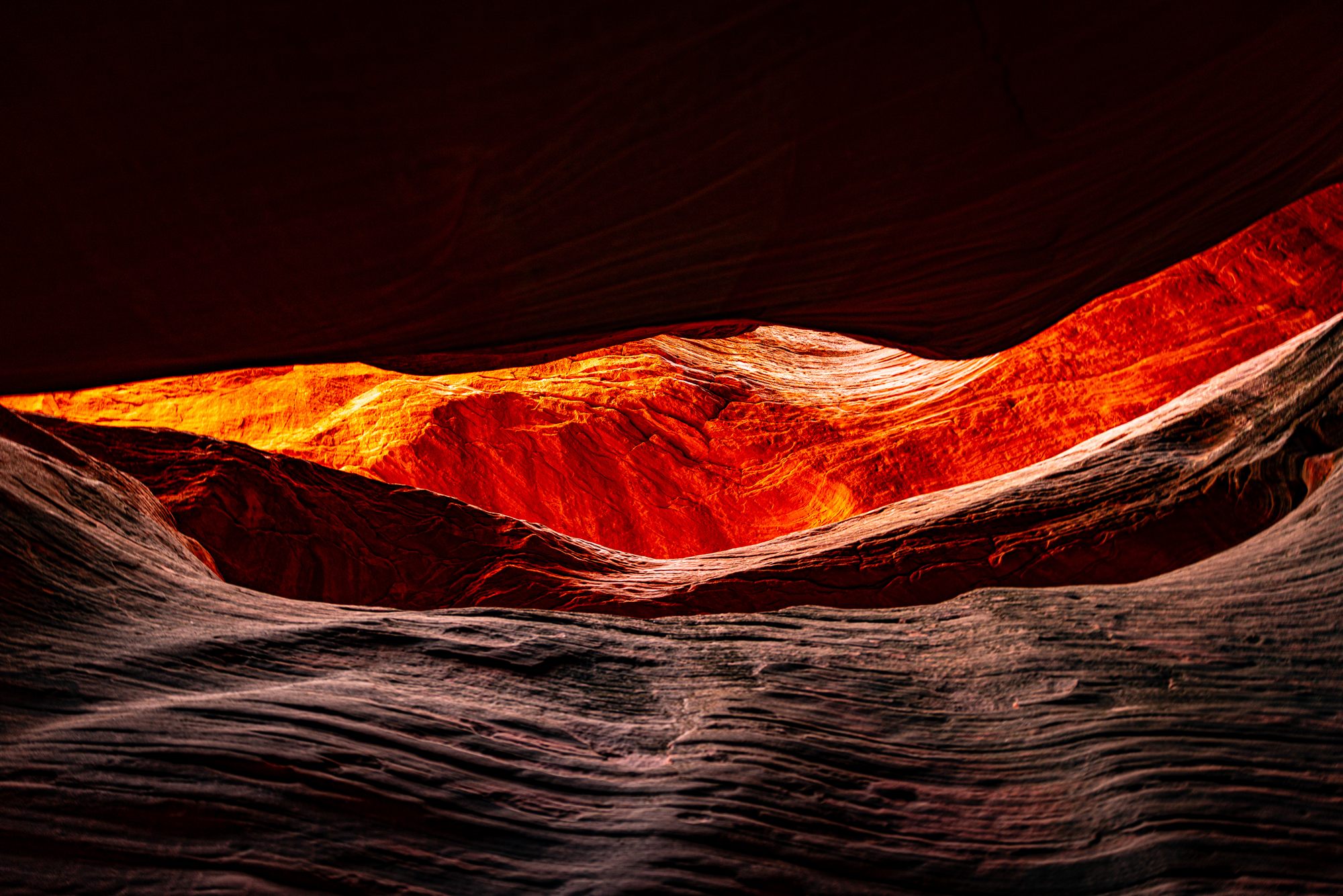 Rippled grey sandstone in shadow before a hollow of glowing red rock