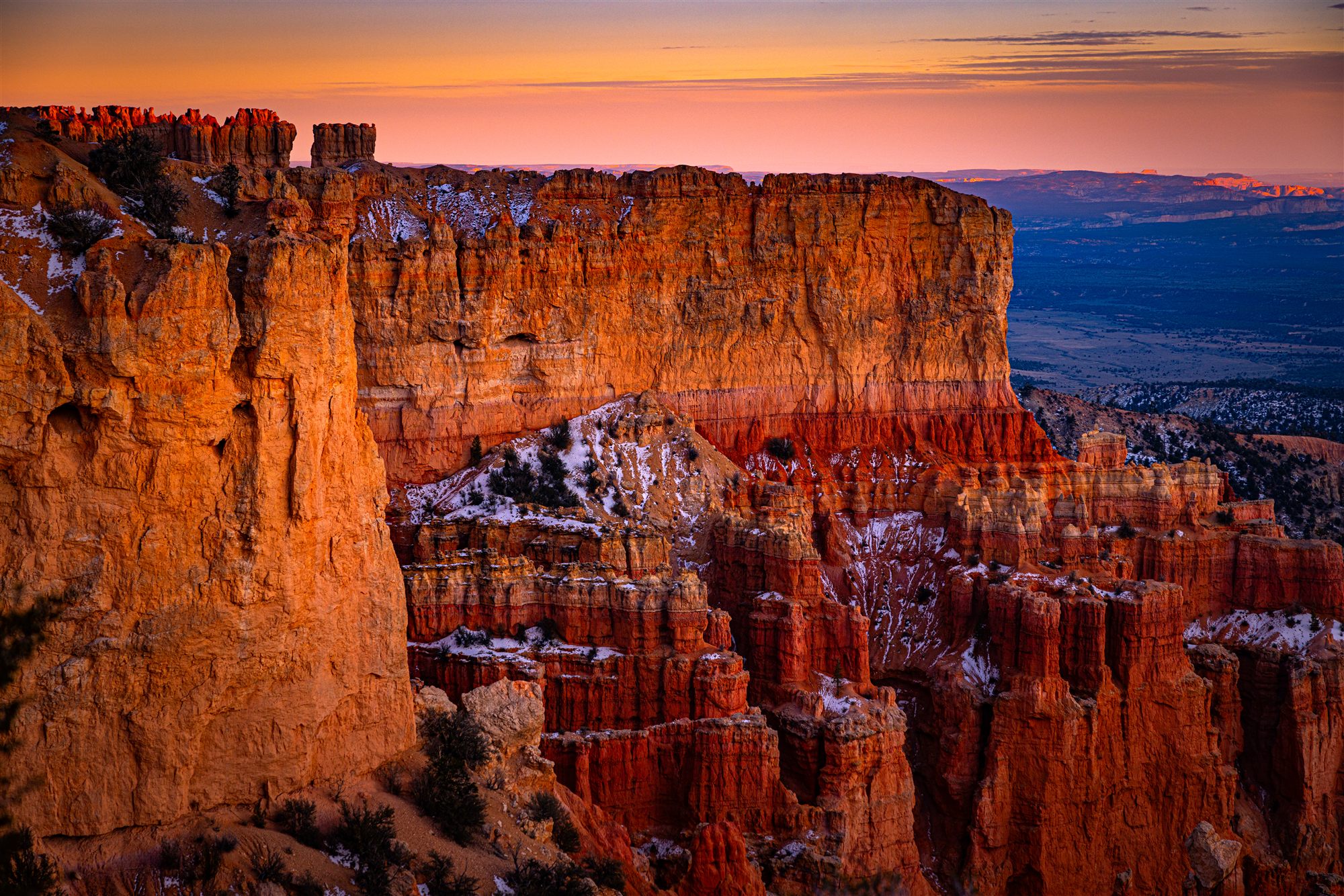 Bryce Canyon hoodoos glowing orange at dusk, snow resting in the shadows below a pink sky