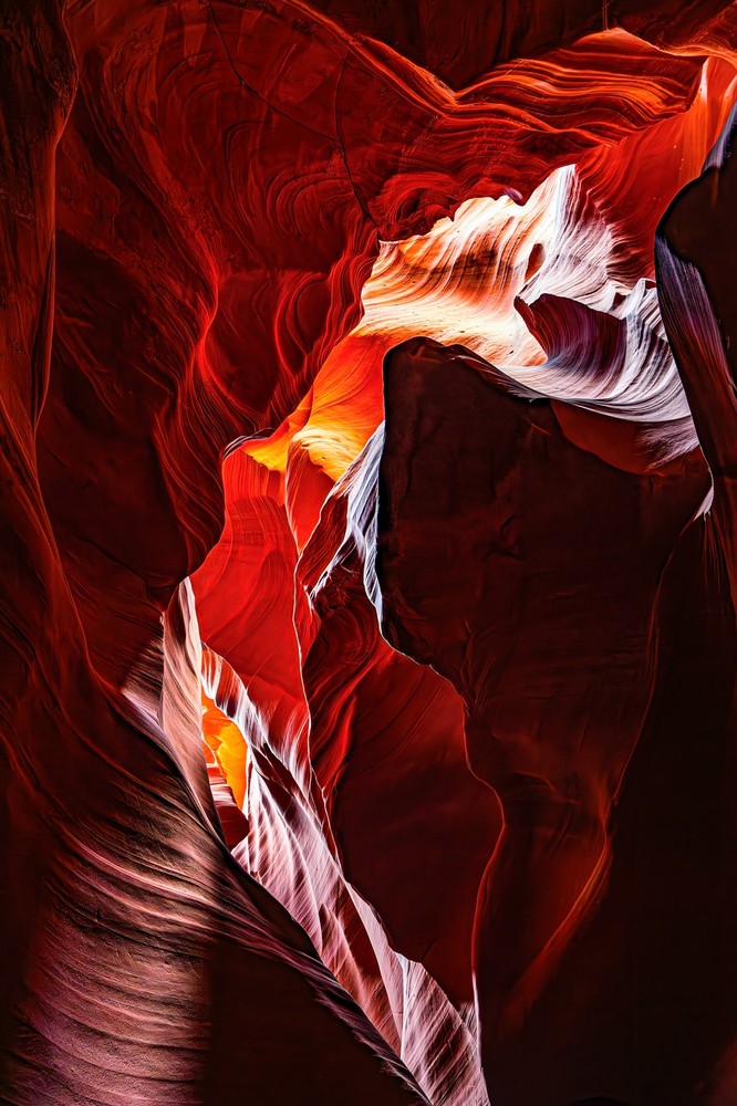 Abstract slot canyon walls in deep red, a silky white and orange wave of sandstone crossing the frame, warm light glowing from below